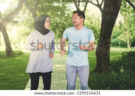 Picture of happy couple wearing sportswear while jogging together in the park