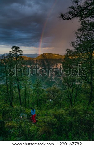 copper canyon with rainbow behind the hills and a woman walking along the sidewalk