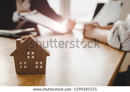customer signing contract for buying house with real estate broker in estate agent office behind wooden house model, investment, home loan contract, real estate, insurance, buy and sell house concept