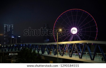 Modern architecture. Evening view of Hong Kong downtown featuring observation wheel. Cityscape fragment with high-rise buildings and glowing round structure.