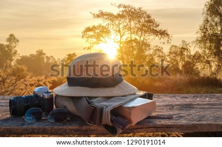 tourism concept picture of hat, book, camera and sun glasses on wooden table in the evening summer sunset.  