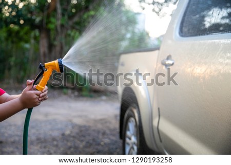 Happy asian child girl help parent washing car on water splashing with sunlight