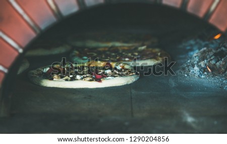 Baking pizzas with cheese and meat in pizza wood oven, selective focus, horizontal composition