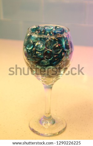 Blue glass circle pieces marbles in wine glass on granite quartz counter top with tile back splash. 