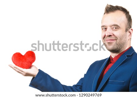 Elegant businessman wearing formal suit holding love symbol, little red heart shaped pillow. Studio shot on isolated background.