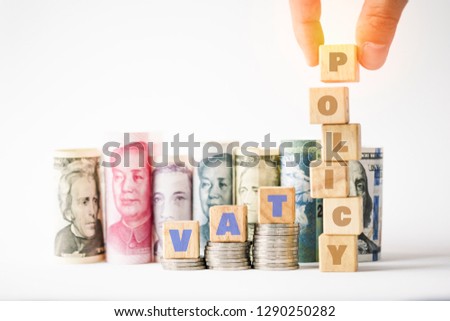 Vat policy keywords on wooden cubes stack on coins and variety banknote background such as Yuan US dollar.Vat policy in each countries concept.