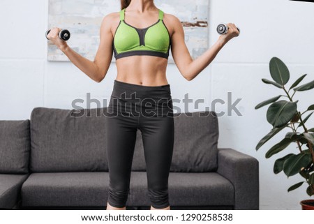 partial view of sportswoman exercising with dumbbells at home