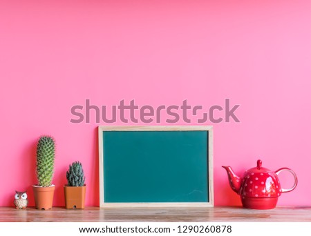 Beautiful  cactus,green  board,red  teapot  and  simulated  owl  on  wooden  surface  with  pink  background