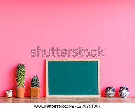 Beautiful  cactus,green  board and  simulated  owl  on  wooden  surface  with  pink  background