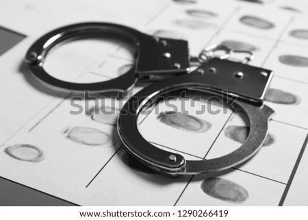Police handcuffs and criminal fingerprints card on table, closeup Royalty-Free Stock Photo #1290266419