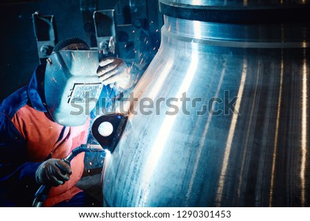 Industrial worker at the plant makes welding for valves of the gas and oil industry close-up. Industrial background.