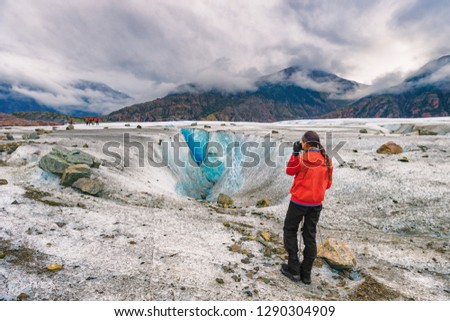 Alaska glacier hike walk tour woman tourist hiker taking pictures on cruise ship excursion helicopter ride. Girl walking on blue ice wilderness nature, popular activity in Alaska holidays.