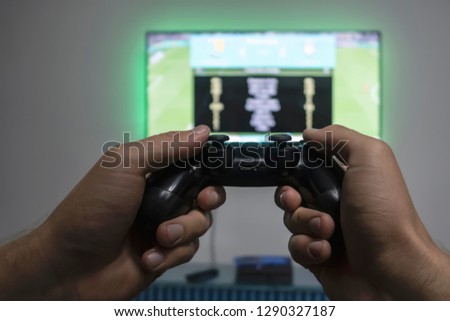 Man playing video game. Hands holding console controller. Football or soccer game on the television. Widescreen tv hangs on the wall