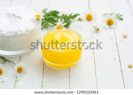 yellow calendula medical cream and white moisturizer with flowers on bright wooden table background