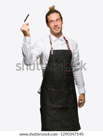 Barber man in an apron holding a credit card and thinking on isolated background