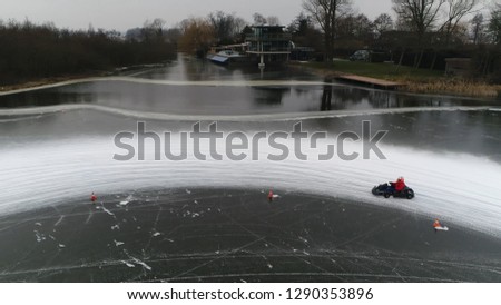 Low altitude aerial photo of go-kart cornering over frozen lake track moving sideways left through corner winter sports activity