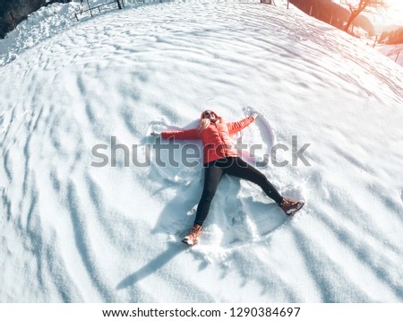 Happy girl making the angel shape on fresh snow - Young woman having fun on high mountains during winter vacation - Holiday and travel concept - Focus on her body