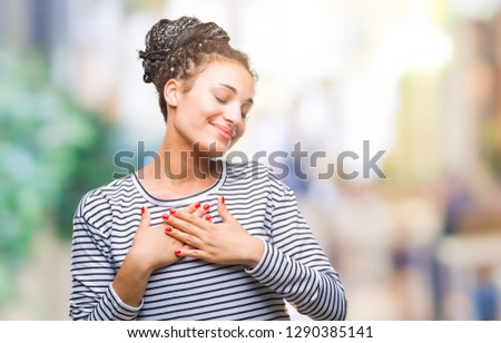 Young braided hair african american girl wearing sweater over isolated background smiling with hands on chest with closed eyes and grateful gesture on face. Health concept.