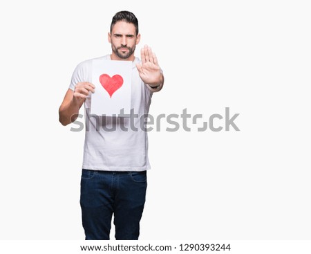 Handsome young man holding card with red heart over isolated background with open hand doing stop sign with serious and confident expression, defense gesture