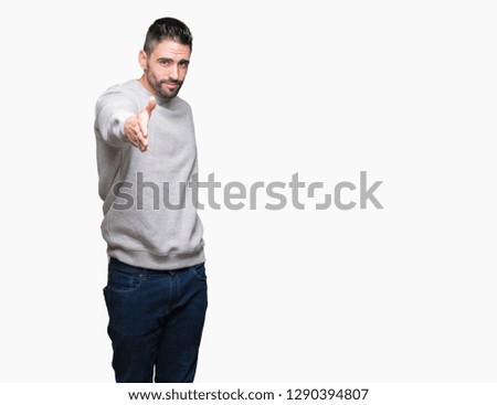 Young handsome man wearing sweatshirt over isolated background smiling friendly offering handshake as greeting and welcoming. Successful business.