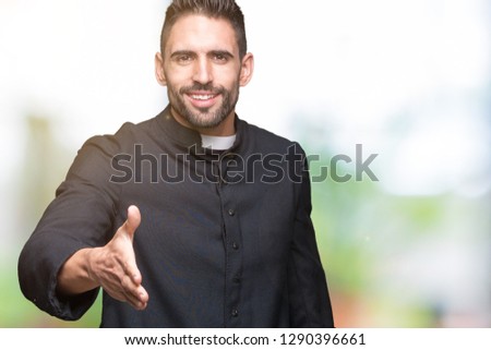 Young Christian priest over isolated background smiling friendly offering handshake as greeting and welcoming. Successful business.