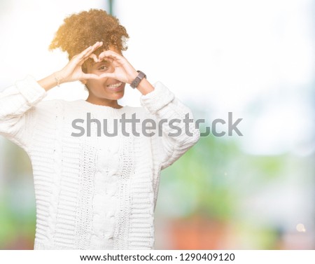 Beautiful young african american woman wearing winter sweater over isolated background Doing heart shape with hand and fingers smiling looking through sign