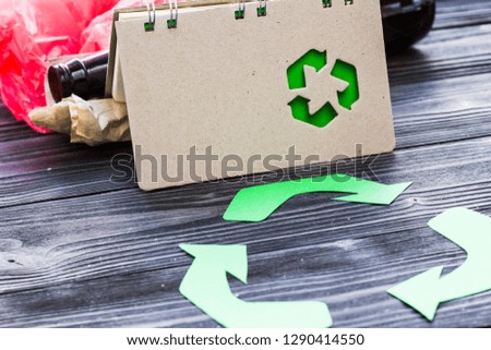 Environmental protection, ecology and recycling concept, recycle sign, notepad and garbage on dark wooden background top view closeup