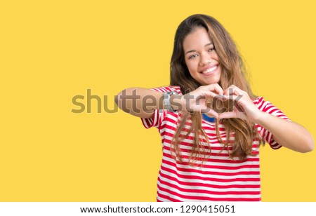 Young beautiful brunette woman wearing stripes t-shirt over isolated background smiling in love showing heart symbol and shape with hands. Romantic concept.
