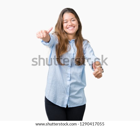 Young beautiful brunette business woman over isolated background approving doing positive gesture with hand, thumbs up smiling and happy for success. Looking at the camera, winner gesture.