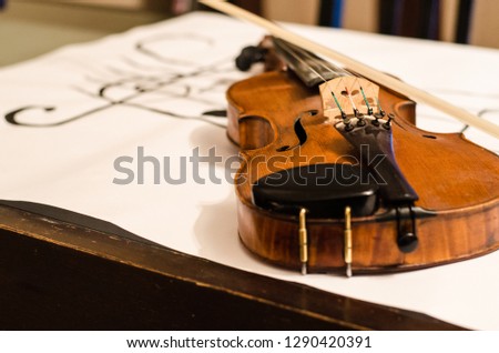 Close up of Violin body with bow positioned in a diagonal over a musical stave drawing with a G-clef with musical notes on a white background placed on a table