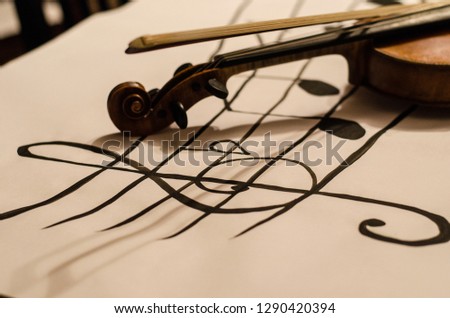 Close up of Violin handle with bow positioned in a diagonal over a diagonal musical stave drawing with a G-clef with musical notes on a white background