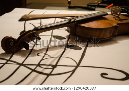 Close up of Violin with bow with focus on it’s handle positioned in a diagonal over a vertical musical stave drawing with a G-clef with musical notes on a white background