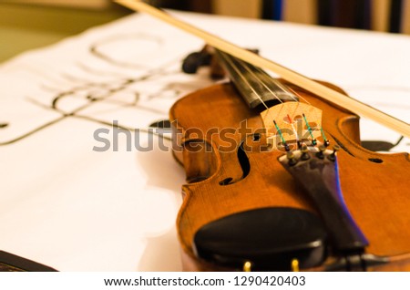 Close up of Violin body with bow positioned in a diagonal over a musical stave drawing with a G-clef with musical notes on a white background