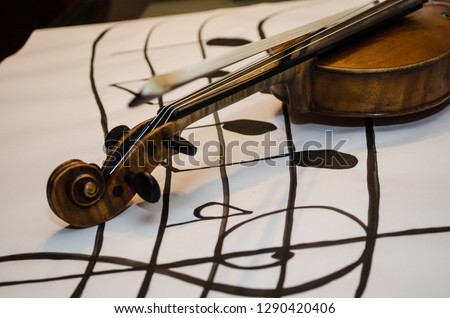 Close up of Violin with bow with focus on it’s handle positioned in a diagonal over a vertical musical stave drawing with a G-clef with musical notes on a white background