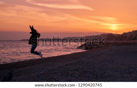 A woman's jumping and having fun by the beach during sunset in Nice, France.