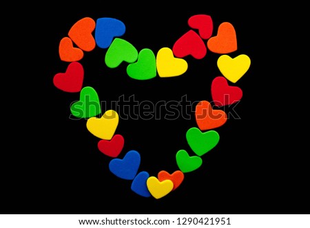 A big heart is laid out of small hearts of blue, red, green, yellow color on a black background. Bright background. Copy space