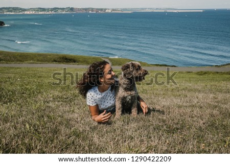 
Young and funny woman playing with her nice spanish water dog on a sunny summer morning in the north of Spain. Lying on the grass overlooking the sea. Lifestyle.