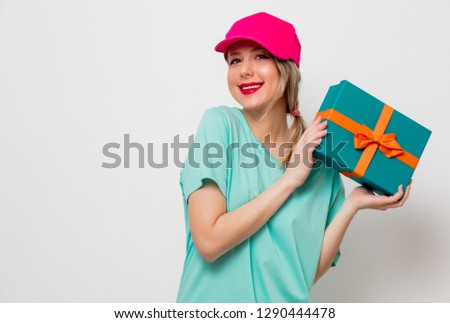 Beautiful young girl in pink cap and blue t-shirt with holiday present box on white background.