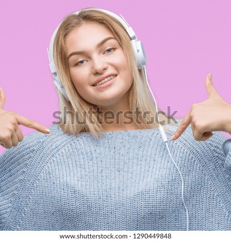 Young caucasian woman listening to music wearing headphones over isolated background looking confident with smile on face, pointing oneself with fingers proud and happy.