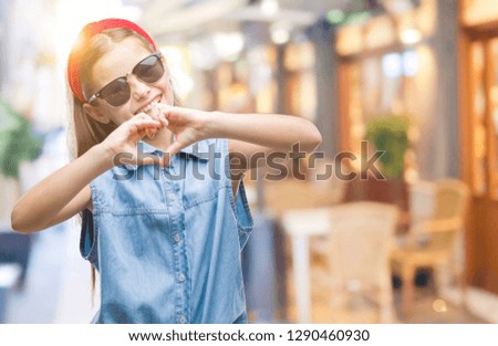 Young beautiful girl wearing sunglasses over isolated background smiling in love showing heart symbol and shape with hands. Romantic concept.