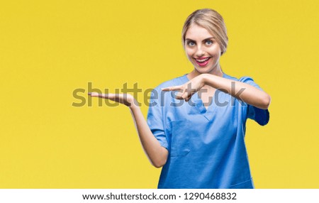 Young beautiful blonde doctor surgeon nurse woman over isolated background amazed and smiling to the camera while presenting with hand and pointing with finger.