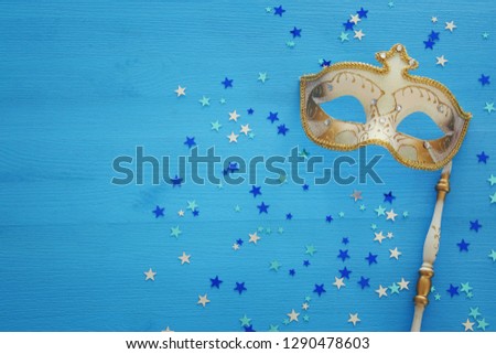 carnival party celebration concept with elegant gold mask on stick over blue wooden background and stars. Top view