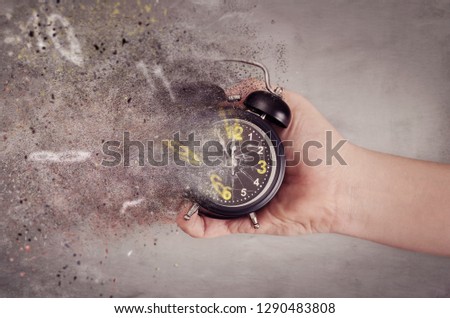 Time is running out concept. The clock breaks down into pieces. Hand holding analog clock with dispersion effect.