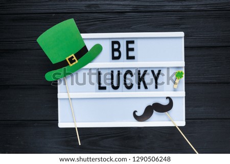 Lightbox with title Be lucky and photobooth green hat and and orange beard on wooden sticks. Creative background to St. Patricks Day