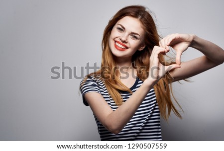 happy red-haired woman with bright makeup and in a striped t-shirt shows the heart with her hands               