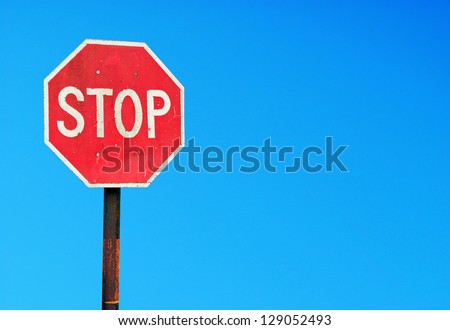 rusty stop sign on a metal pole against a vibrant blue sky (copy-space for your design)