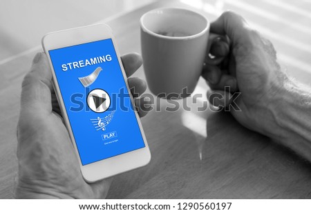 Male hands holding a smartphone with streaming concept and a cup of coffee