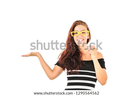 Happy young woman doing a hand gesture to one side while holding a photo booth prop in the shape of yellow glasses against a white background