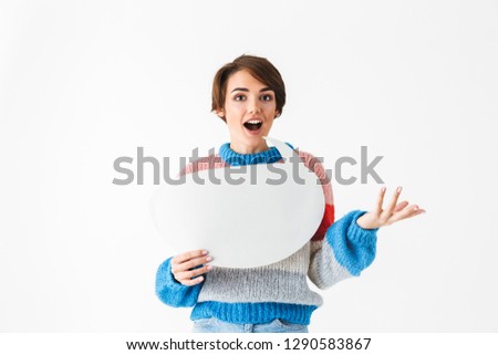 Happy cheerful girl wearing sweater standing isolated over white background, holding empty speech bubble