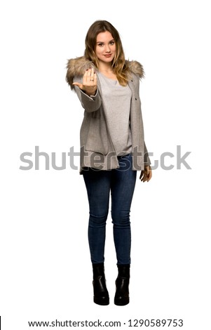 A full-length shot of a Teenager girl with coat inviting to come with hand. Happy that you came on isolated white background
